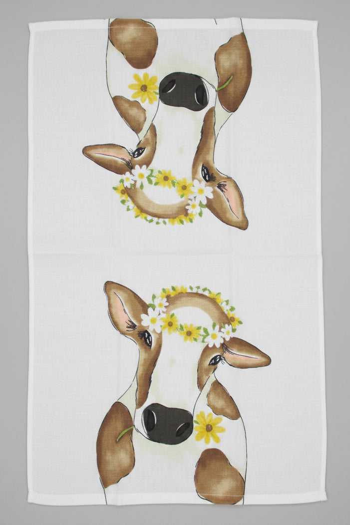 Towel fully opened featuring a printed design of two cow faces wearing yellow flower crowns, laid flat on a gray surface.