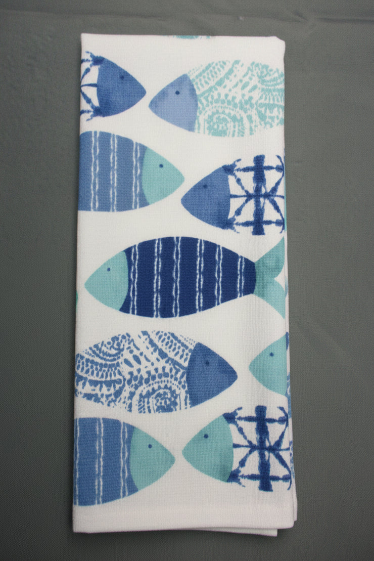 A folded white towel, featuring a repeating pattern of stylized fish in shades of blue, navy, and light teal with various decorative motifs.