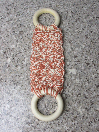 A handmade Kitchen towel Holder made of 100% Cotton Yarn in Rust and Ivory Color with two cream-colored wooden rings, shown on a speckled gray countertop.