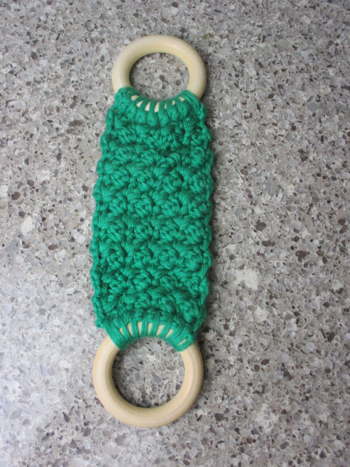 A handmade Kitchen towel Holder made of 100% Cotton Yarn in Bright  Green Color with two cream-colored wooden rings, shown on a speckled gray countertop.