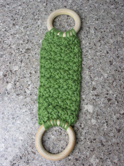 A handmade Kitchen towel Holder made of 100% Cotton Yarn in Olive  Green Color with two cream-colored wooden rings, shown on a speckled gray countertop.