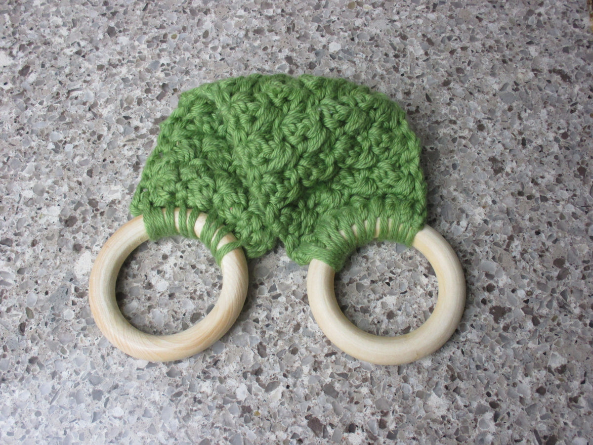A handmade Kitchen towel Holder made of 100% Cotton Yarn in Olive  Green Color with two cream-colored wooden rings, shown on a speckled gray countertop.