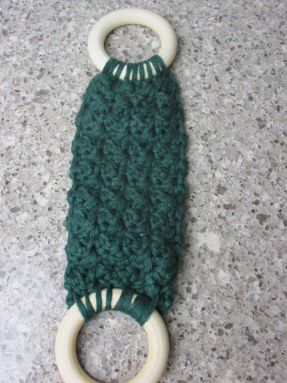 A handmade Kitchen towel Holder made of 100% Cotton Yarn in Forest Green Color with two cream-colored wooden rings, shown on a speckled gray countertop.
