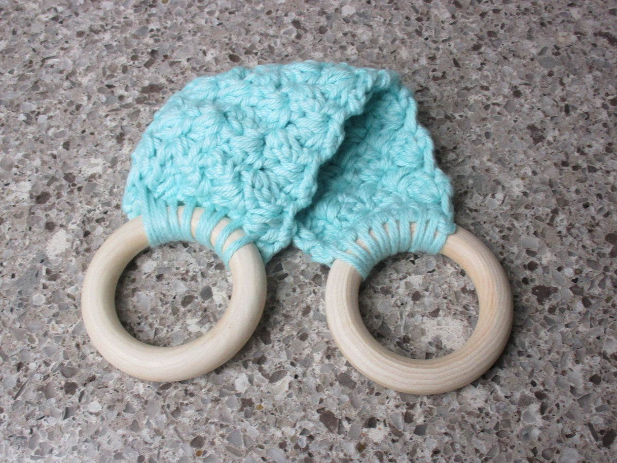 A handmade Kitchen towel Holder made of 100% Cotton Yarn in Med. Aqua Color with two cream-colored wooden rings, shown on a speckled gray countertop.