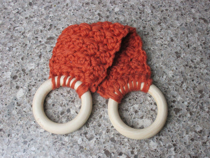 A handmade Kitchen towel Holder made of 100% Cotton Yarn in Rust Color with two cream-colored wooden rings, shown on a speckled gray countertop.