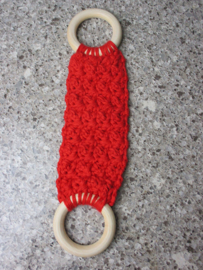 A handmade Kitchen towel Holder made of 100% Cotton Yarn in Bright Red Color with two cream-colored wooden rings, shown on a speckled gray countertop.