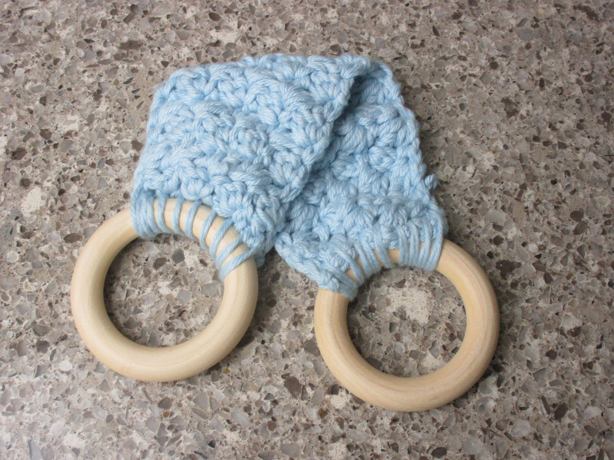 A handmade Kitchen towel Holder made of 100% Cotton Yarn in Soft Blue Color with two cream-colored wooden rings, shown on a speckled gray countertop.