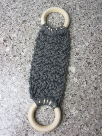 A handmade Kitchen towel Holder made of 100% Cotton Yarn in Dk. Gray Color with two cream-colored wooden rings, shown on a speckled gray countertop.