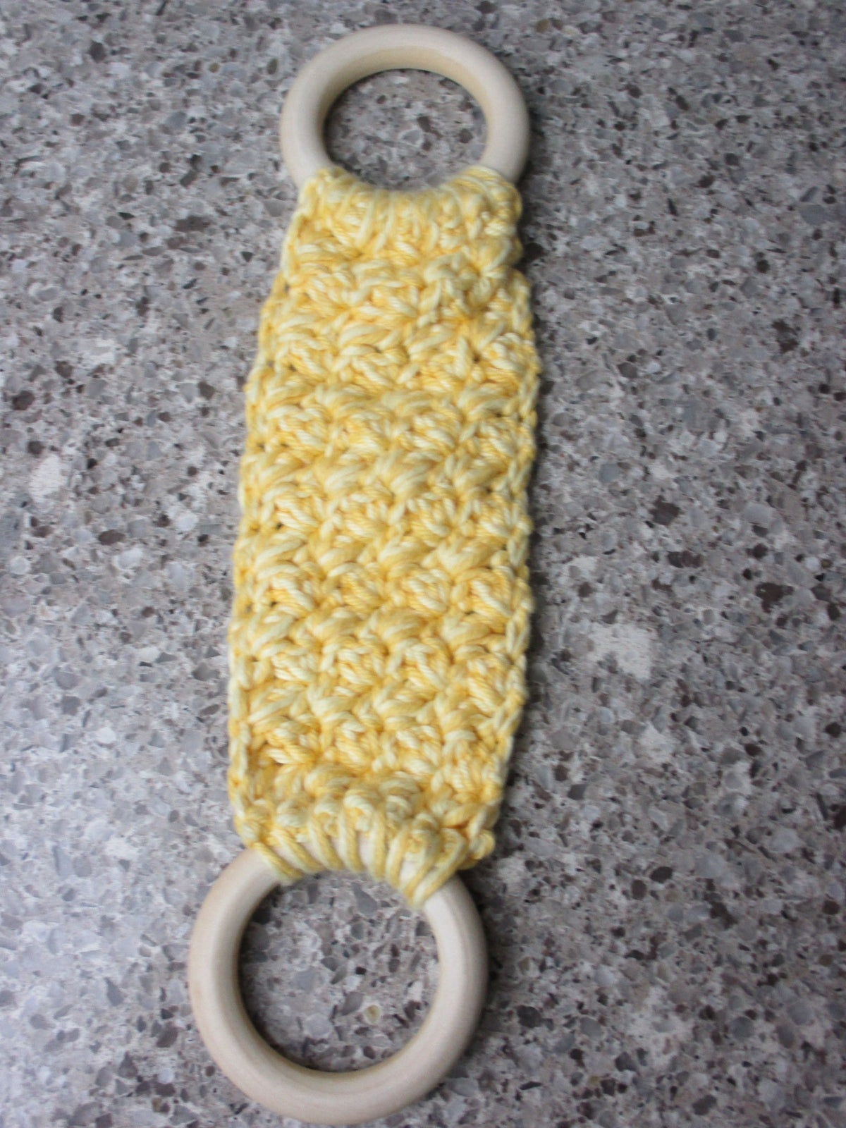 A handmade Kitchen towel Holder made of 100% Cotton Yarn in Yellow and Lt. Yellow Colors with two cream-colored wooden rings, shown on a speckled gray countertop.