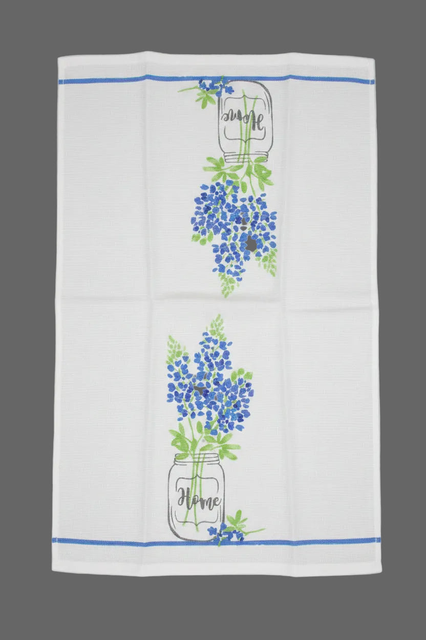 A white kitchen tea towel with blue and green floral designs in mason jar vases and blue border stripes, laid flat on a dark gray background.