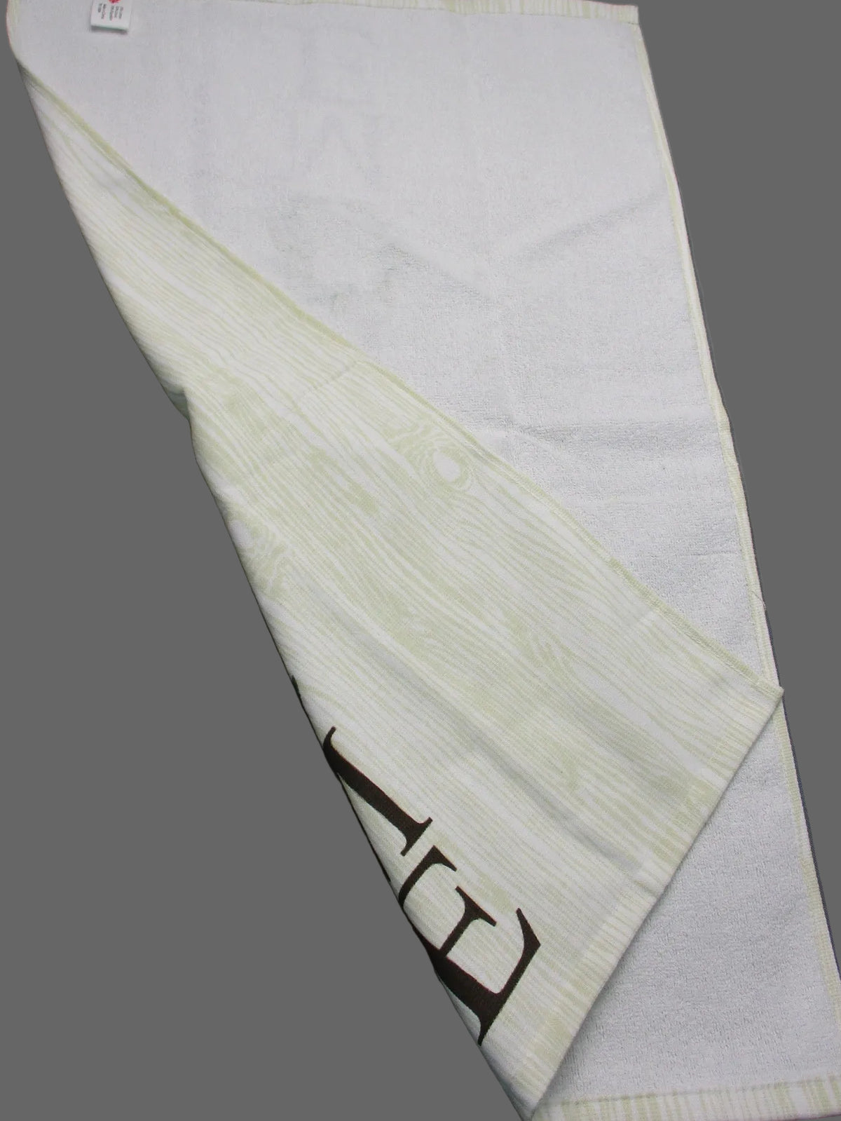 Back side of towel with a subtle textured pattern and a dark brown printed logo, laid out on a gray surface.