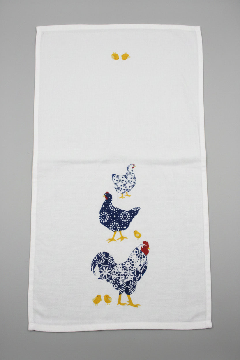 A white fabric towel featuring  chickens and chicks in navy, white, and yellow, laid opened flat on a gray surface.