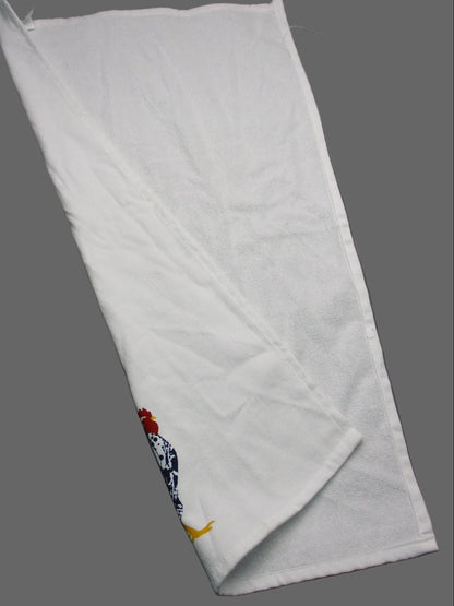Back side of towel laid on a dark gray surface. The bottom-right corner is folded over to reveal a small design featuring a red and yellow bird motif on a blue patterned section.