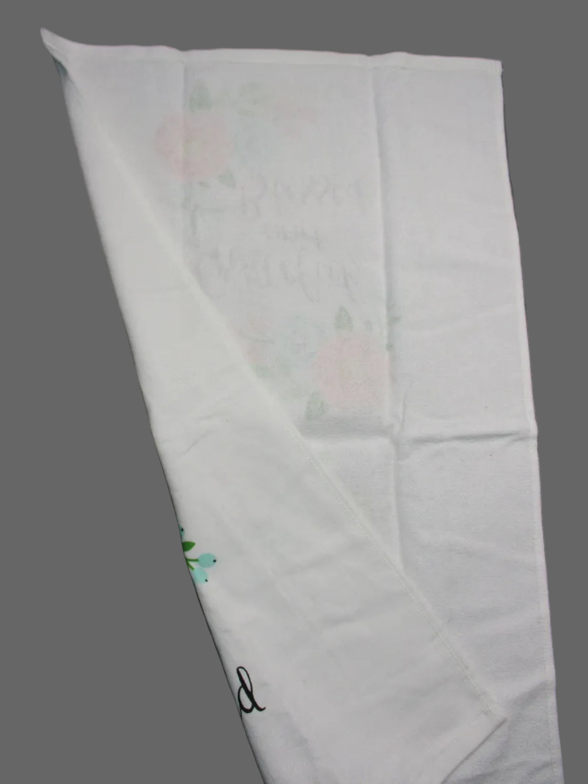 Back side of towel with a faded pink floral pattern and cursive writing, folded diagonally on a dark gray surface.