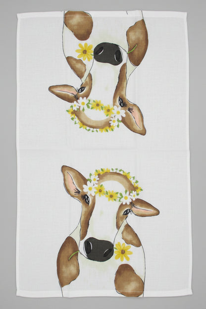Towel fully opened featuring a printed design of two cow faces wearing yellow flower crowns, laid flat on a gray surface.