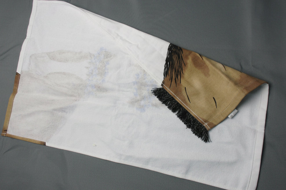 Back side of towel, featuring a printed brown and black graphic on one corner, laid out on a gray textured surface.