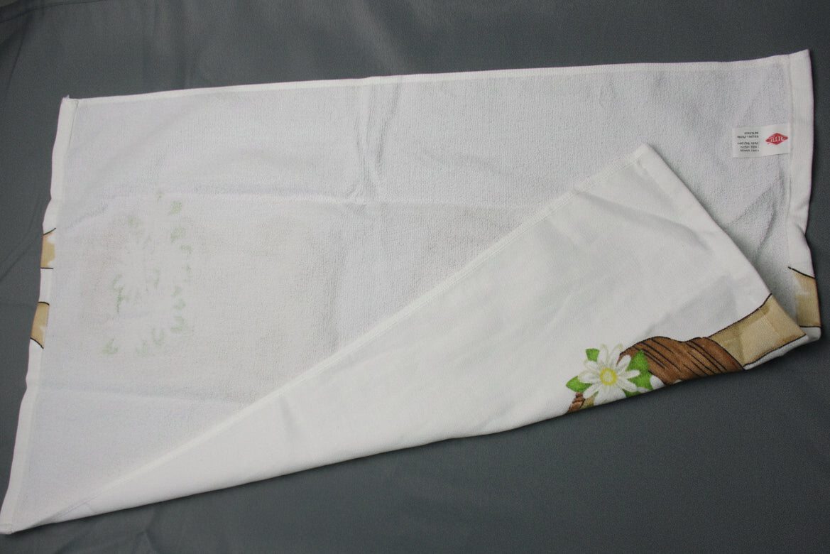 Back side of towel with a small floral and leaf print in the bottom right corner, folded over on a dark gray fabric background.