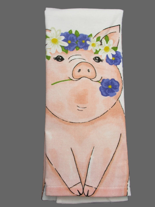 A folded white towel, printed with a cute cartoon pig wearing a blue and white flower crown, laid flat on a dark gray background.