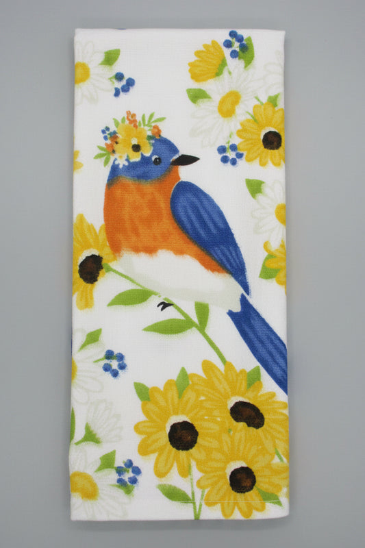 A folded white towel, featuring a colorful print of a bluebird, yellow sunflowers, and small white daisies on a dark gray background.