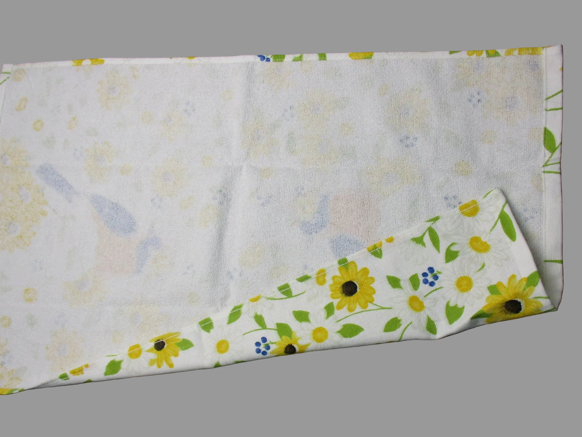 Back side of towel, featuring a floral print with yellow sunflowers, green leaves, and small blue accents. The fabric is laid flat on a dark gray surface with a metal ruler visible on the right edge.