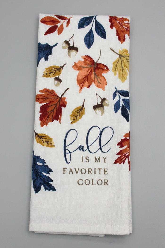A folded white kitchen towel, printed with autumn leaves in orange, red, yellow, and blue, acorns, and the text 'fall is my FAVORITE COLOR' on a dark gray background.