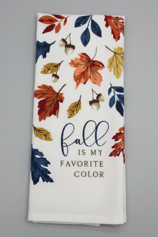 A folded white kitchen towel, printed with autumn leaves in orange, red, yellow, and blue, acorns, and the text 'fall is my FAVORITE COLOR' on a dark gray background.