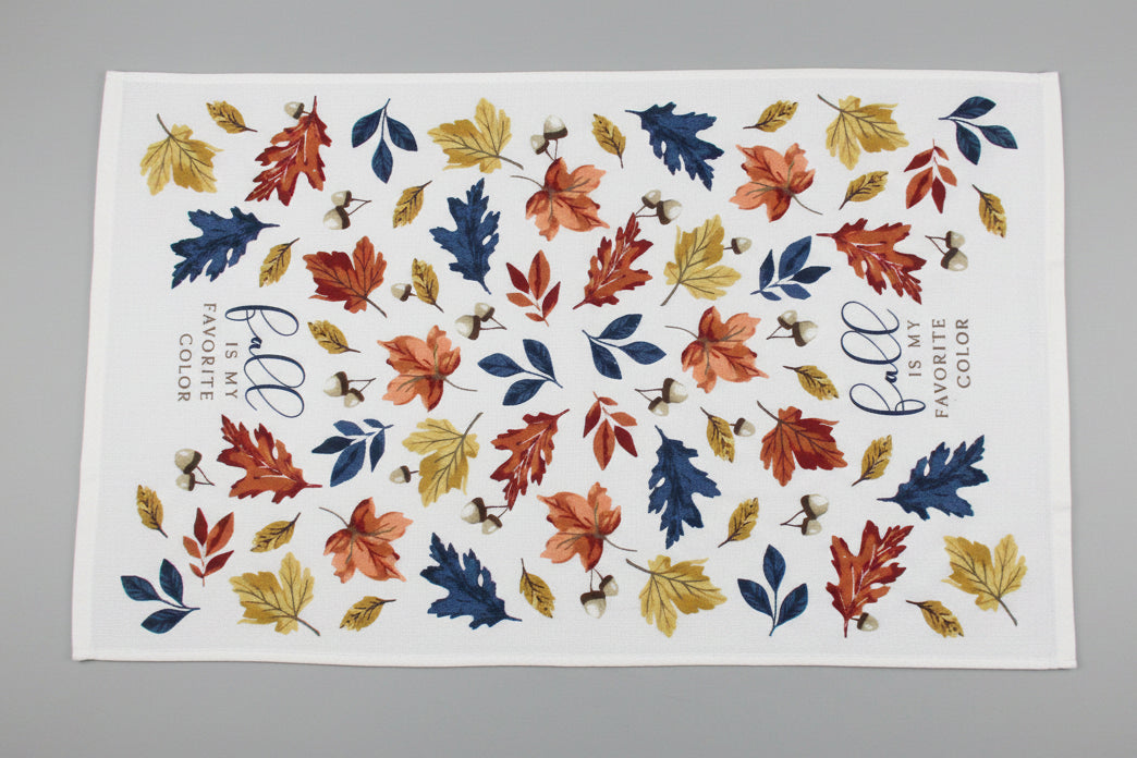 A white towel fully opened featuring an autumn leaf pattern in orange, red, yellow, and blue, with the phrase 'fall is my FAVORITE COLOR' printed on it, laid flat on a gray surface.