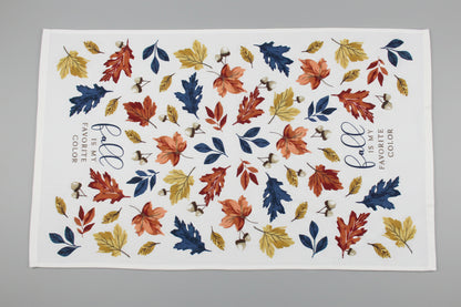 A white towel fully opened featuring an autumn leaf pattern in orange, red, yellow, and blue, with the phrase 'fall is my FAVORITE COLOR' printed on it, laid flat on a gray surface.