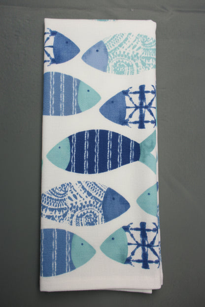 A folded white towel, featuring a repeating pattern of stylized fish in shades of blue, navy, and light teal with various decorative motifs.