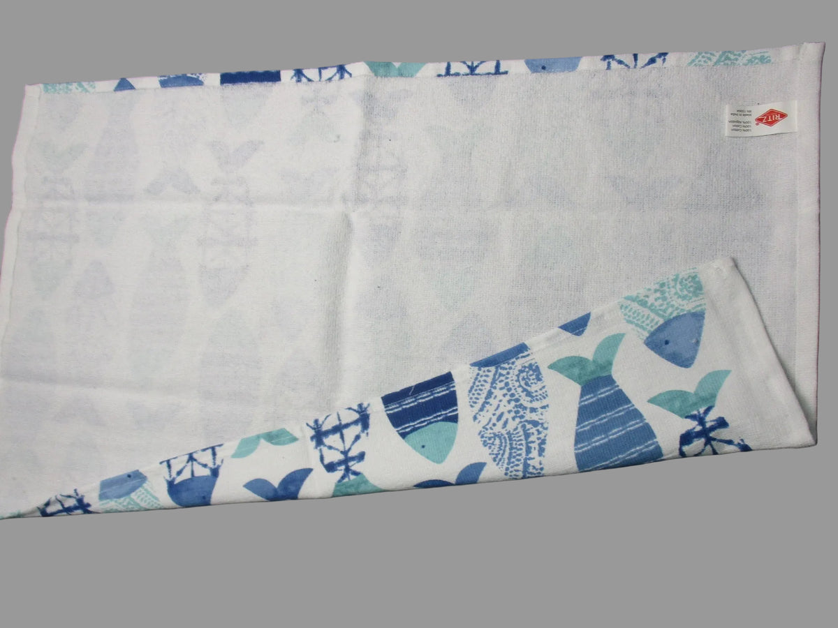 Back side of towel with a blue fish and nautical pattern, laid flat on a gray surface with one corner folded over.