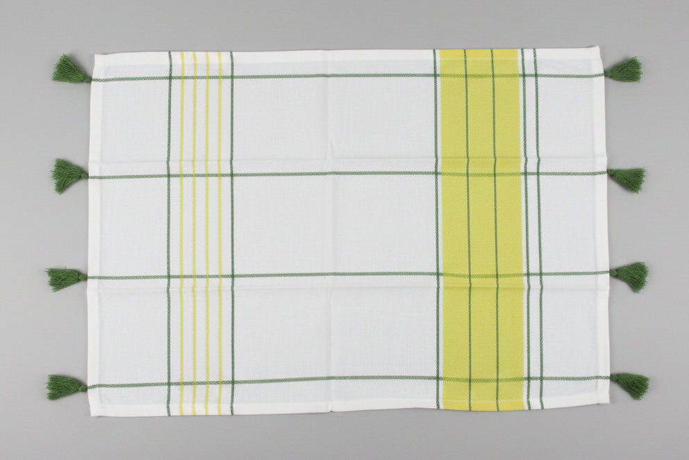 A white kitchen towel open fully with a green and yellow striped pattern and tassels on one side, laid flat on a gray surface.