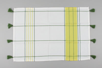 A white kitchen towel open fully with a green and yellow striped pattern and tassels on one side, laid flat on a gray surface.