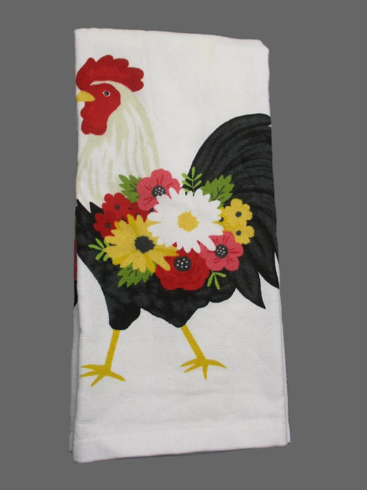 A folded white towel, featuring a graphic print of a rooster with a colorful floral bouquet on its back, laid flat on a dark gray background.
